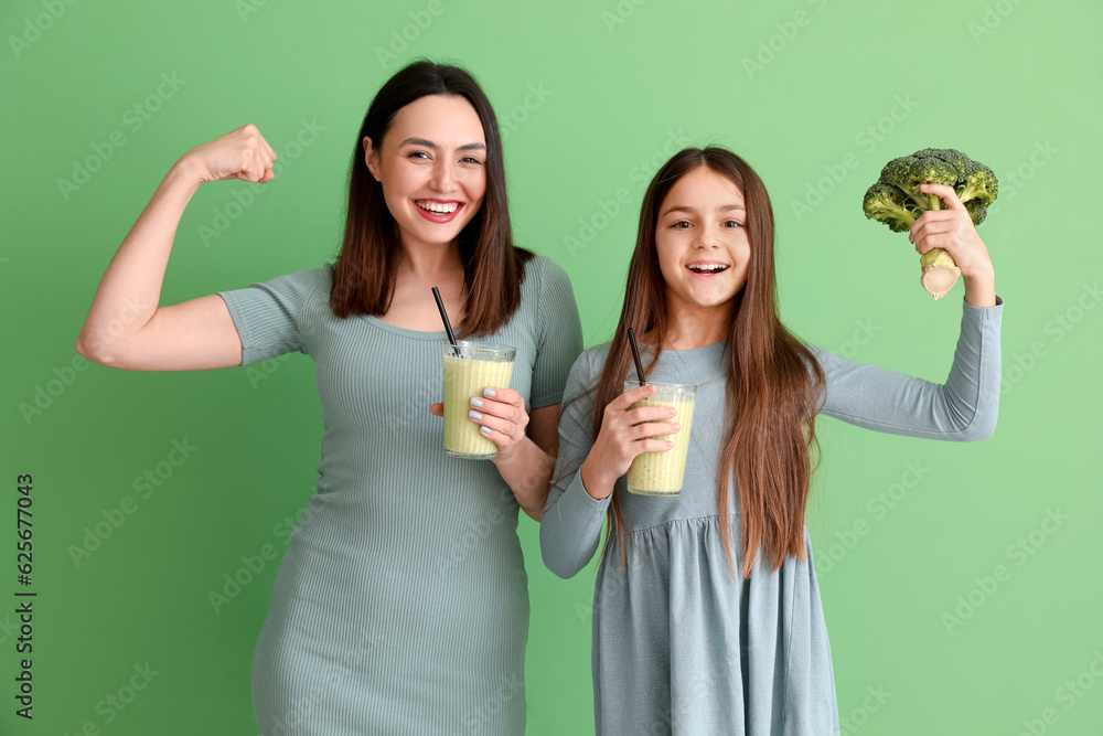 Little girl with broccoli and her mother drinking smoothie on green background