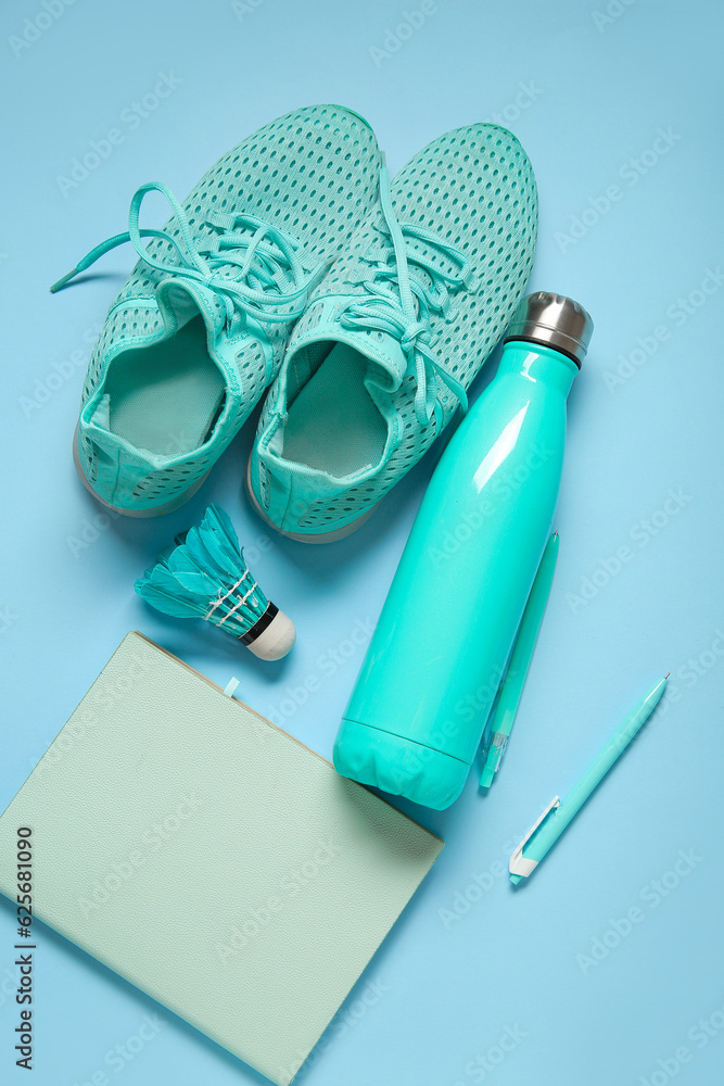 Sneakers with bottle of water, badminton shuttlecock and stationery on blue background