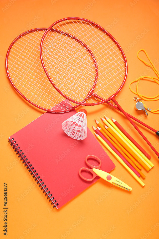 Rackets with badminton shuttlecock, whistle and different stationery on orange background
