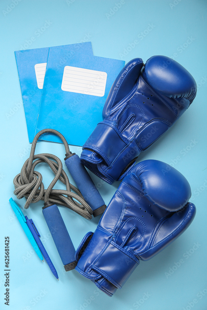 Boxing gloves with skipping rope and different stationery on blue background