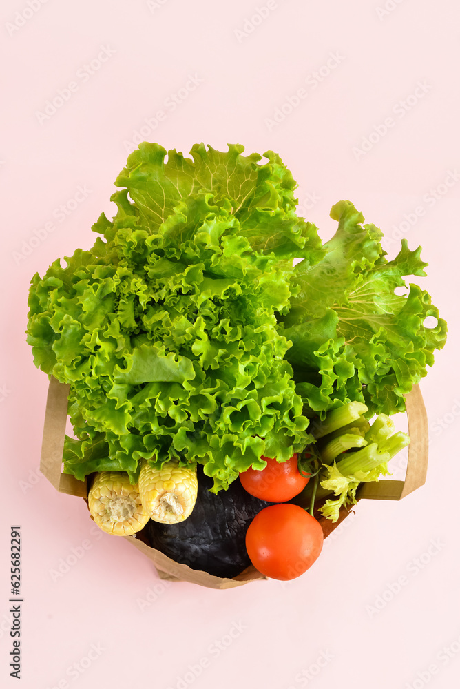 Paper bag with fresh vegetables on pink background. Grocery shopping concept