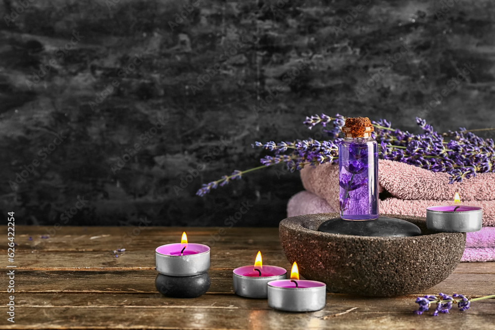 Composition with bottle of essential oil, burning candles and lavender flowers on wooden table