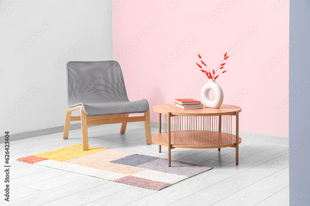 Grey armchair, coffee table and stylish rug near pink wall