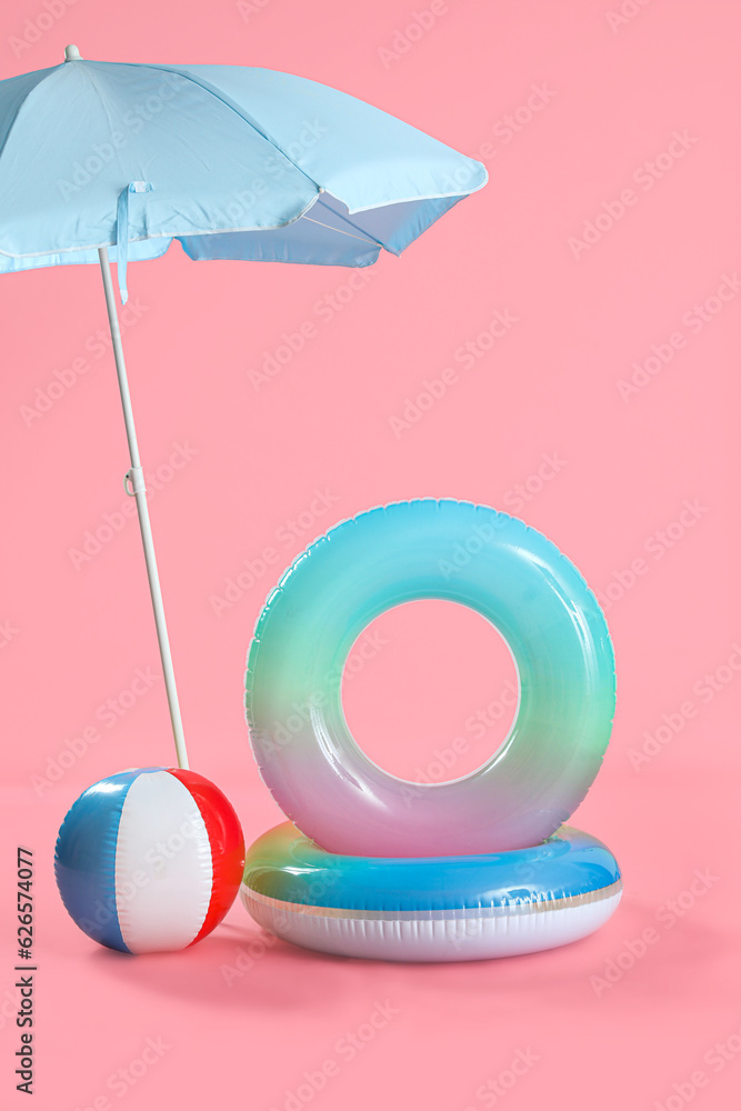Swim rings with beach ball and umbrella on pink background