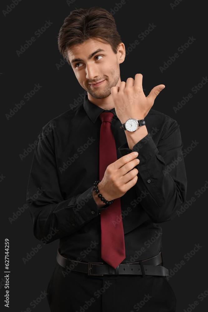 Handsome elegant young man with wristwatch on black background