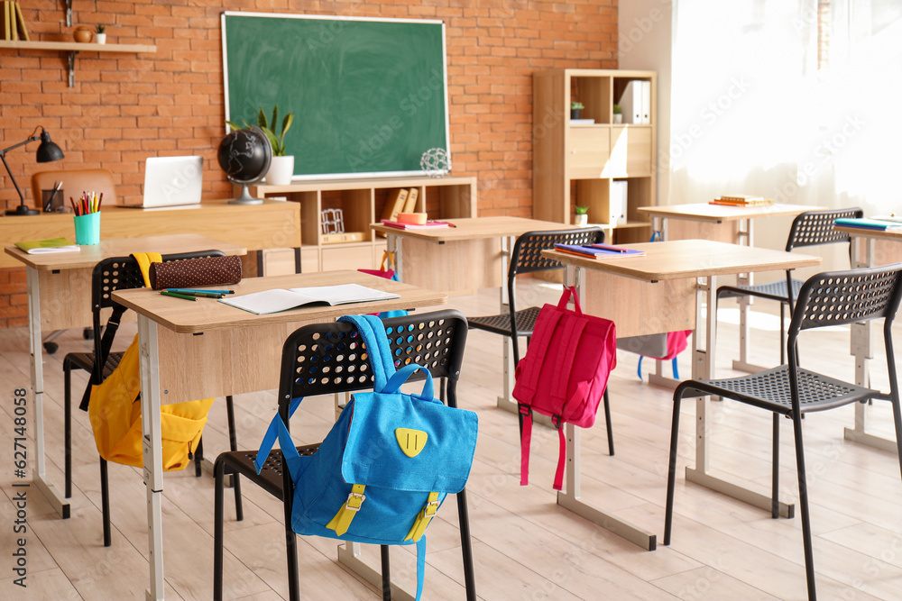 Interior of stylish empty classroom with backpacks and stationery