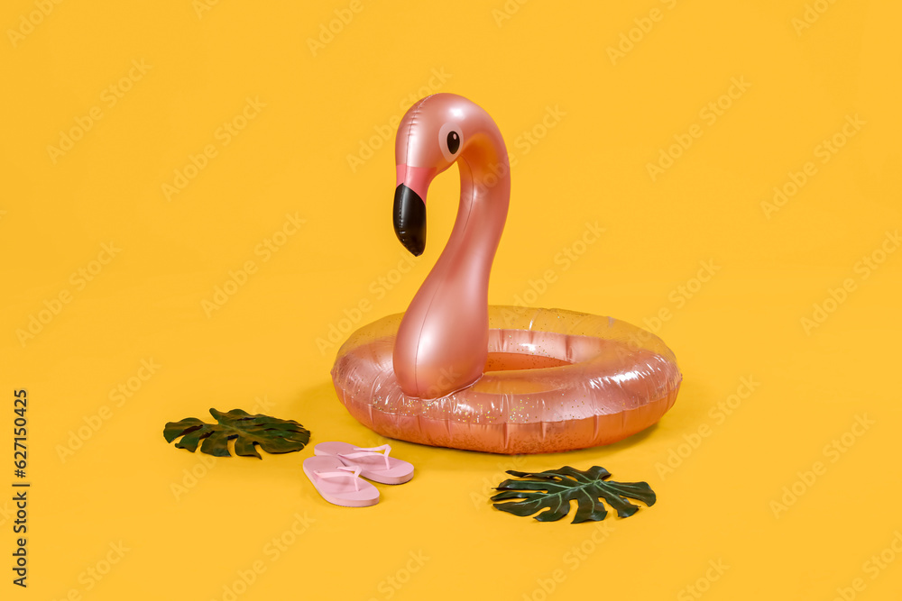 Inflatable ring in shape of flamingo with palm leaves and flip-flops on pink background