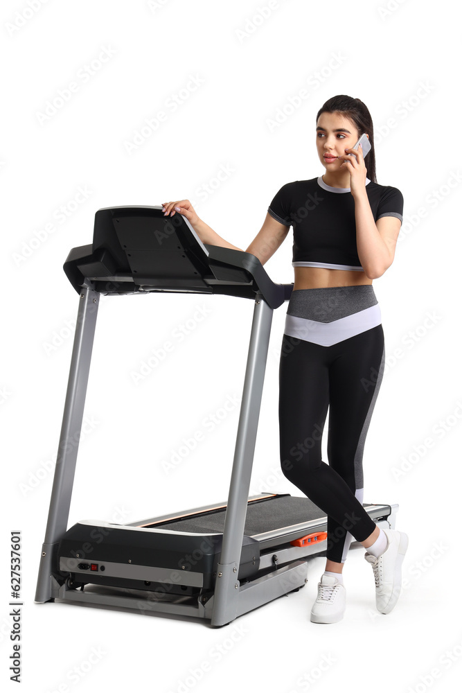 Sporty young woman with treadmill talking by mobile phone on white background