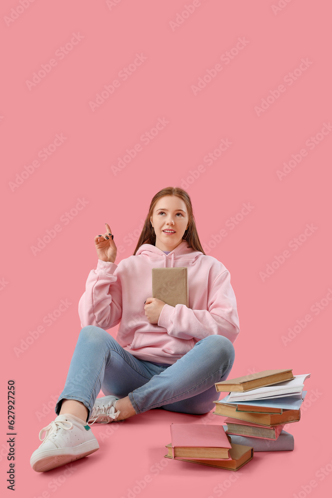 Teenage girl with books pointing at something on pink background