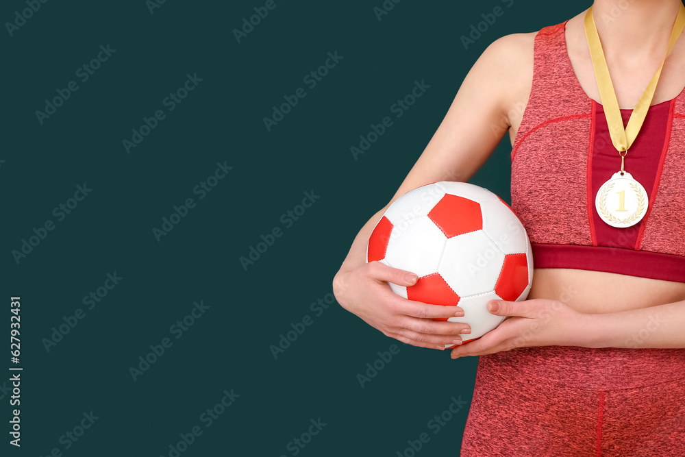 Female football player with first place medal and ball on green background