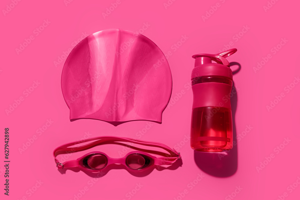 Bottle of water, swimming cap and goggles on color background