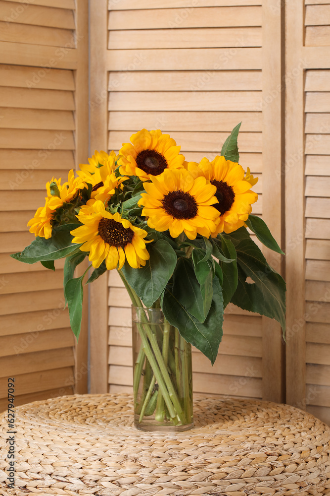 Vase with beautiful sunflowers on wicker mats near folding screen