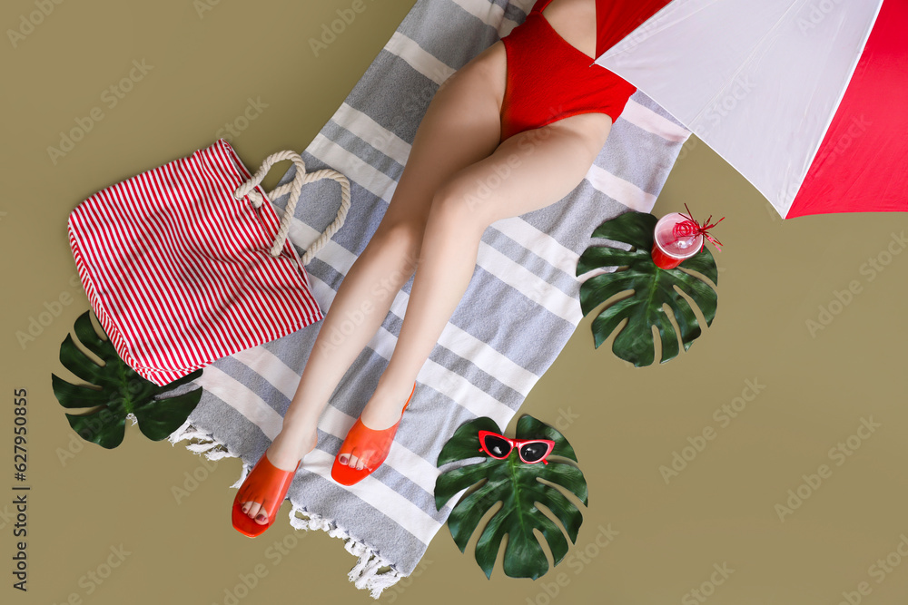 Young woman with cocktail and palm leaves relaxing on green background