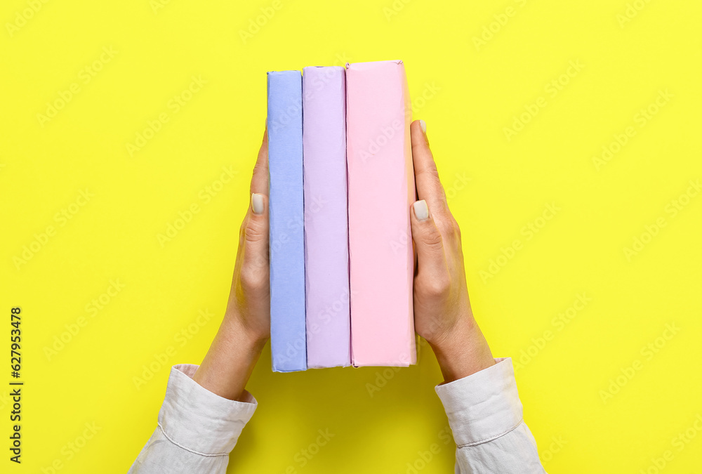 Female hands holding books on yellow background