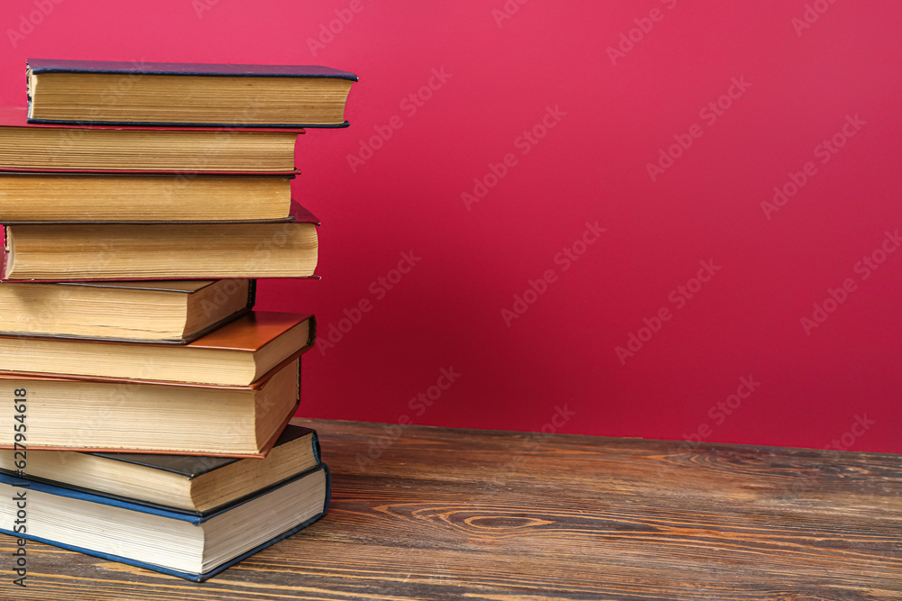 Stack of books on wooden table against red background