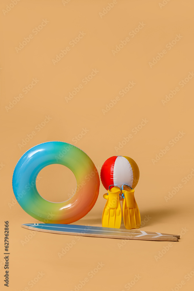 Swim ring with beach ball, flippers and surfboard on beige background