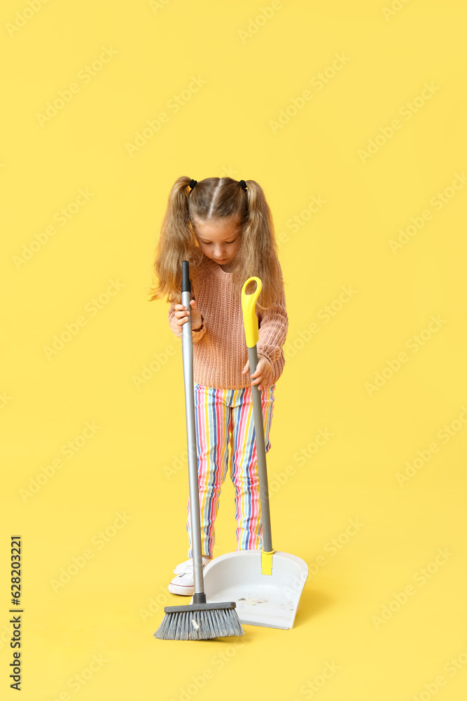 Cute little girl with broom and dustpan on yellow background