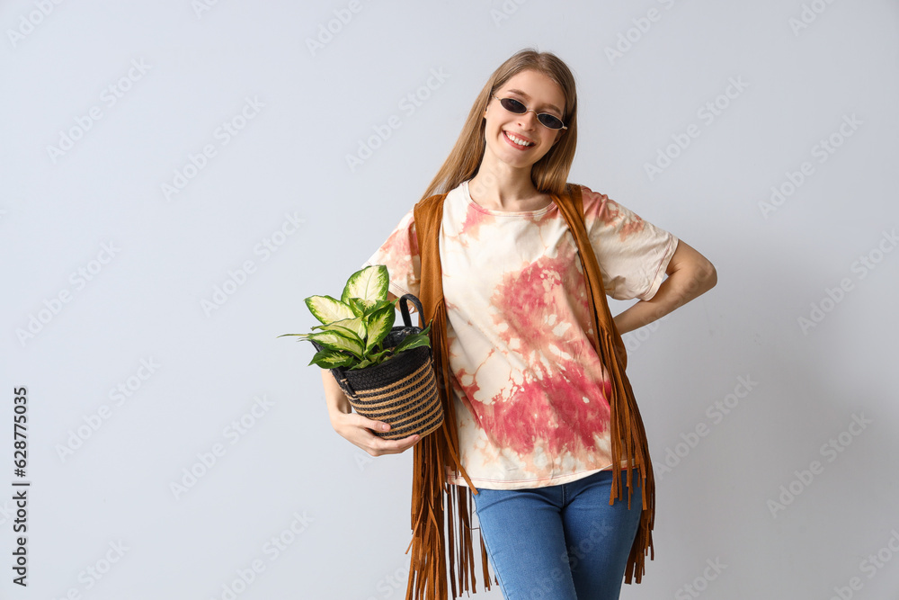 Young woman in tie-dye t-shirt with houseplant on light background