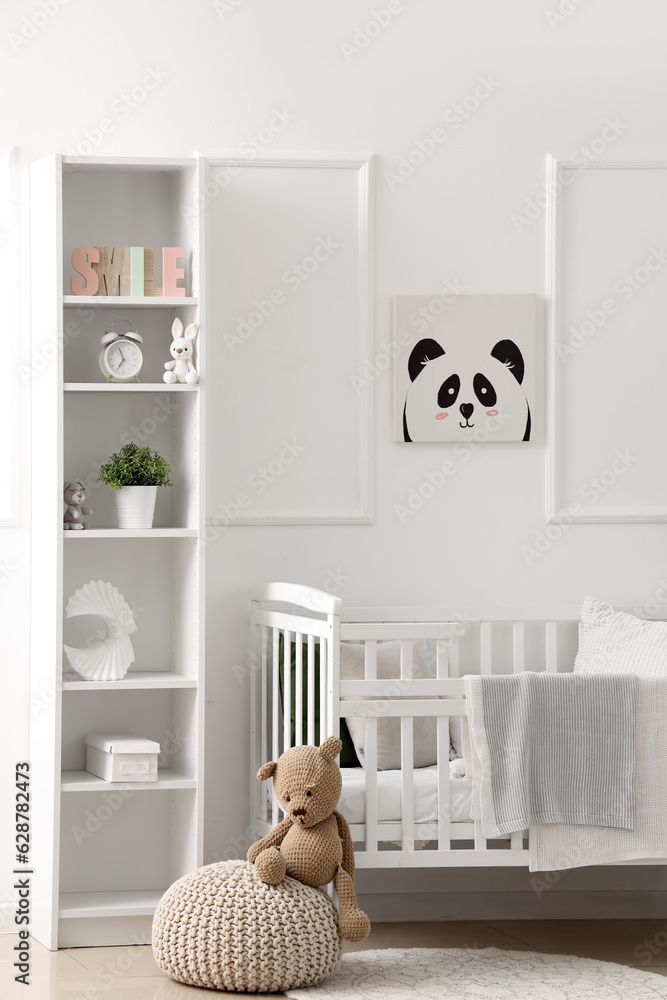 Stylish interior of childrens room in white tones with baby bed and shelving unit