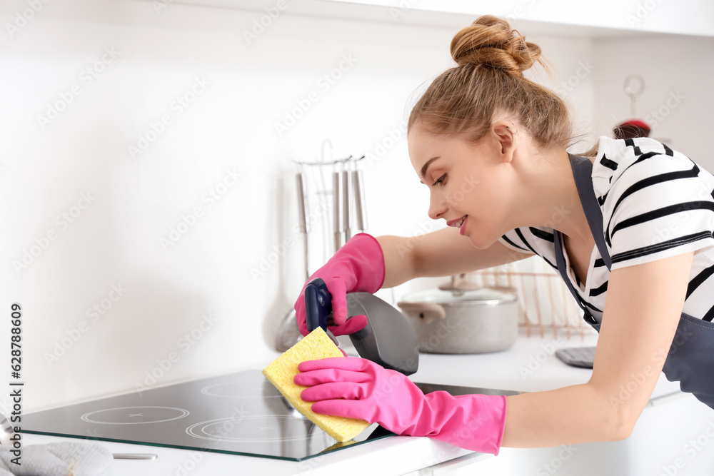 Pretty young woman in pink rubber gloves cleaning electric stove with sponge and detergent