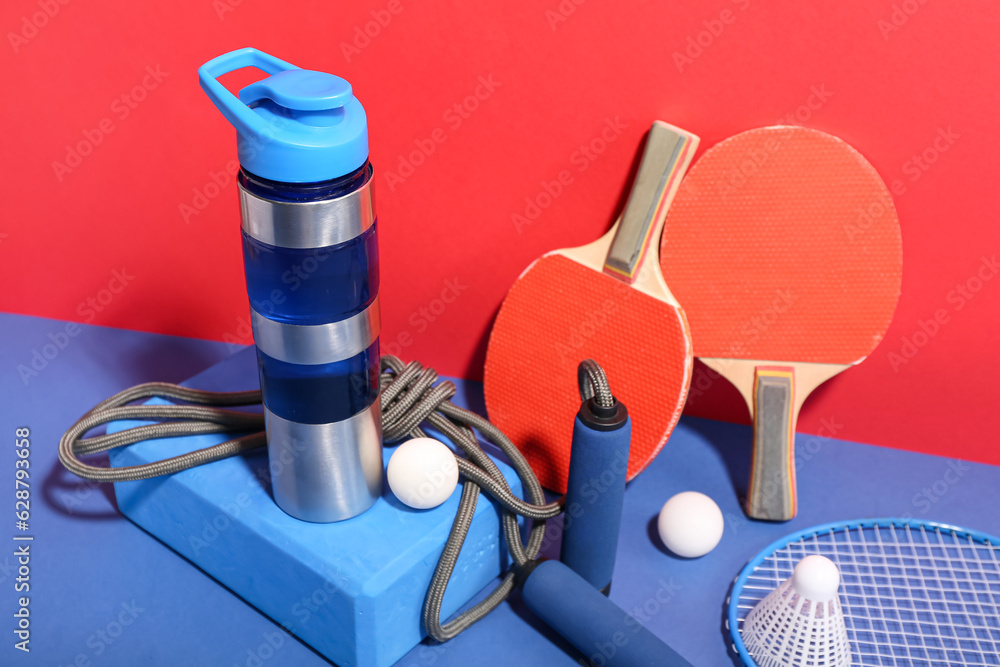 Bottle of water and different sports equipment on color background