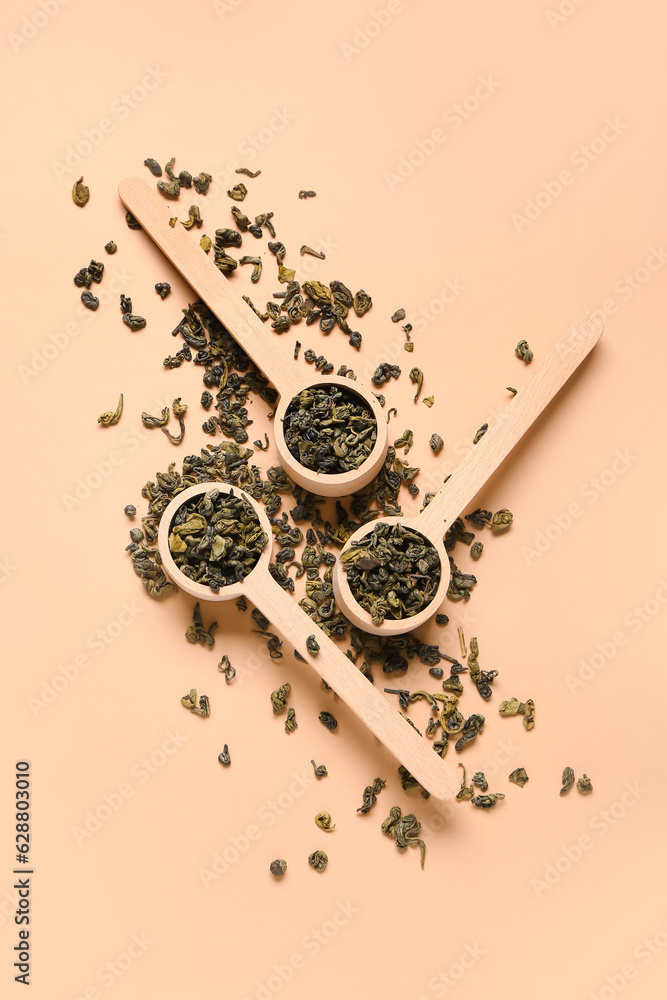 Wooden spoons with dry tea leaves on orange background