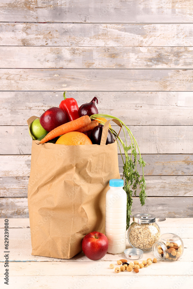 Paper bag with vegetables and fruits on light wooden table