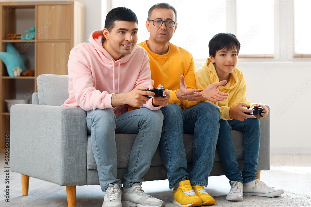 Happy little boy with his dad and grandfather playing video game at home