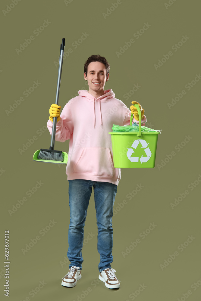 Young man with broom and recycle bin on green background