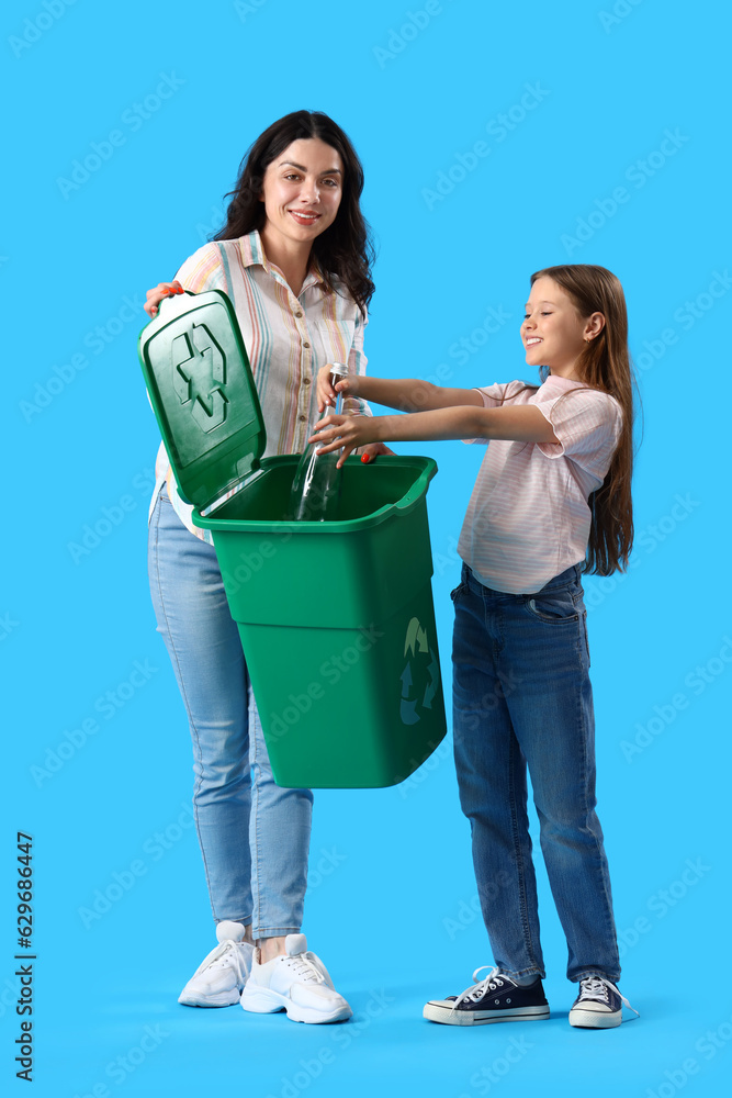 Little girl with her mother throwing glass bottle in recycle bin on blue background