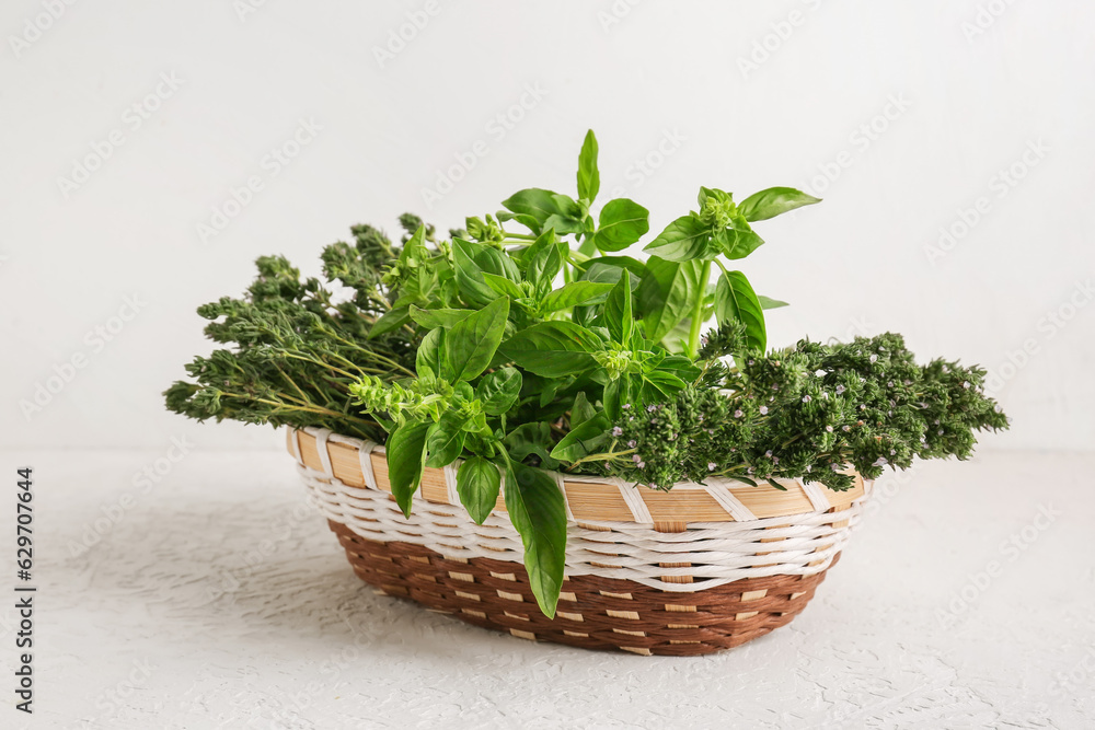 Wicker basket with fresh herbs on light background