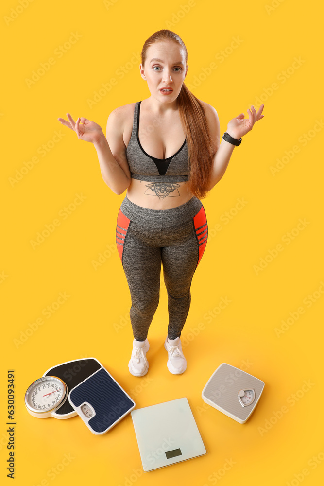 Upset young overweight woman with scales on yellow background