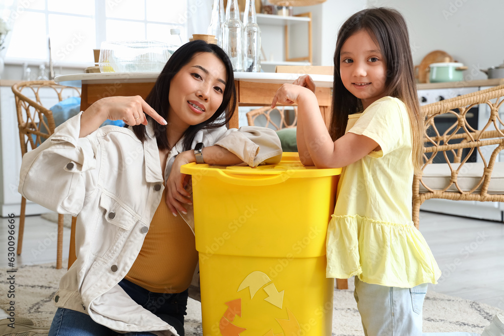Asian mother with her little daughter pointing at recycle bin in kitchen