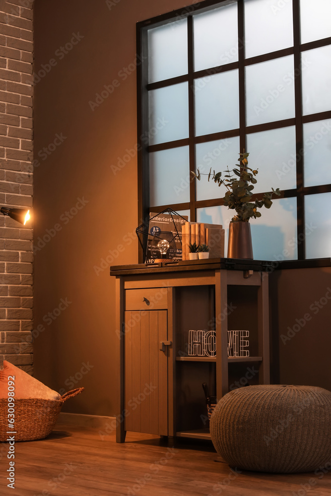 Table with glowing lamp, decor and houseplants in dark living room