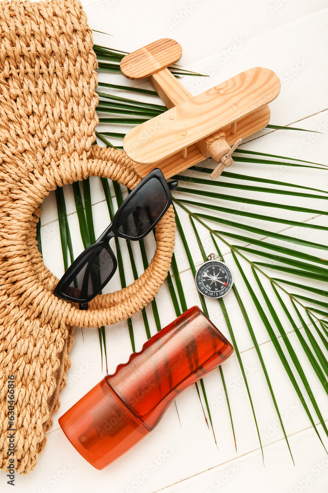 Composition with sunglasses, wicker bag, bottle of sunscreen and palm leaf on white wooden backgroun