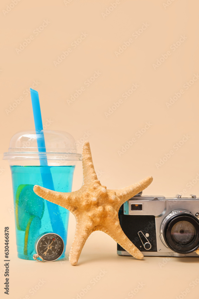 Starfishes, photo camera, compass and plastic cup of blue drink on beige background