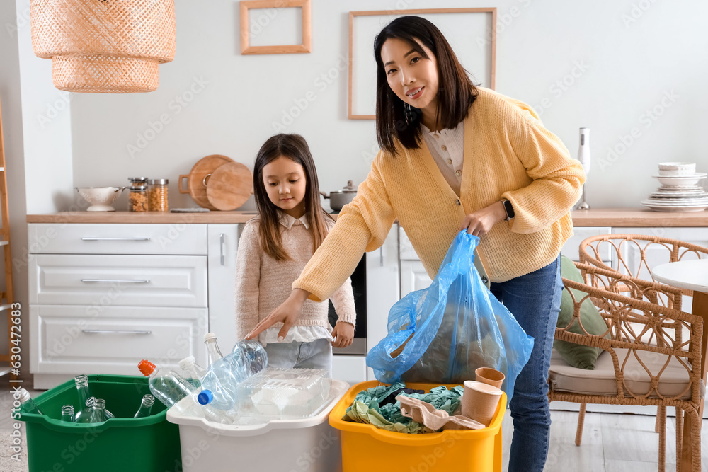 Asian mother with her little daughter sorting garbage with recycle bins in kitchen