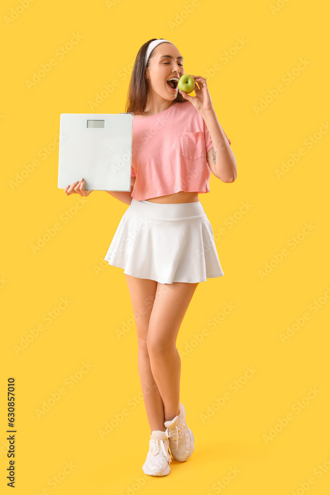 Young woman with scales eating apple on yellow background