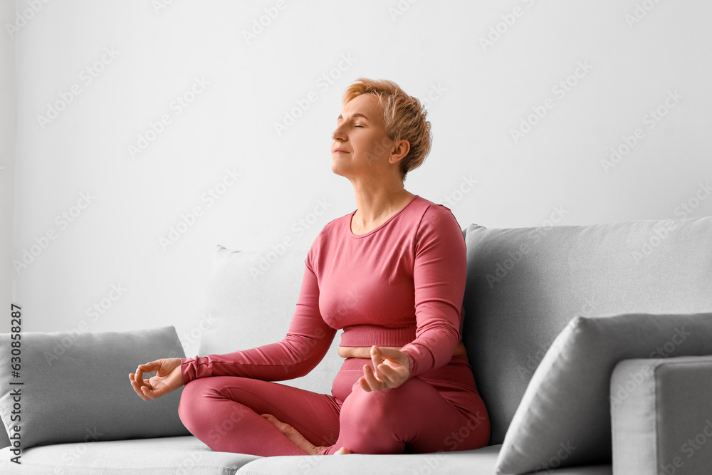 Mature woman meditating while sitting on sofa