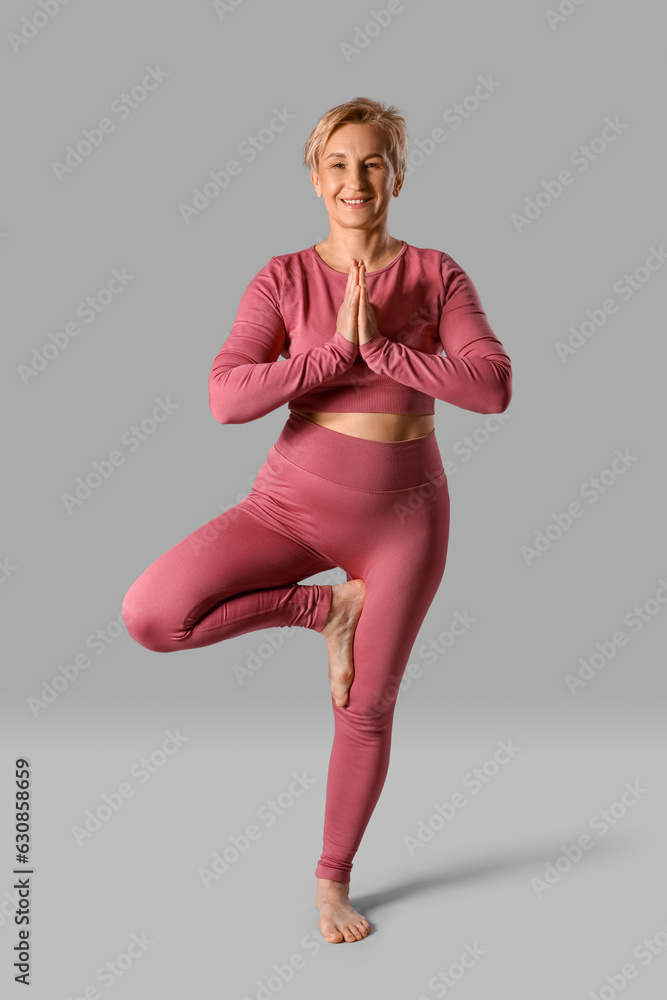 Sporty mature woman practicing yoga on grey background