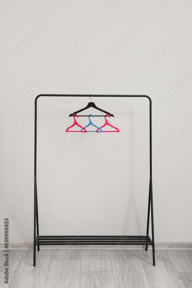 Rack with plastic clothes hangers near grey wall