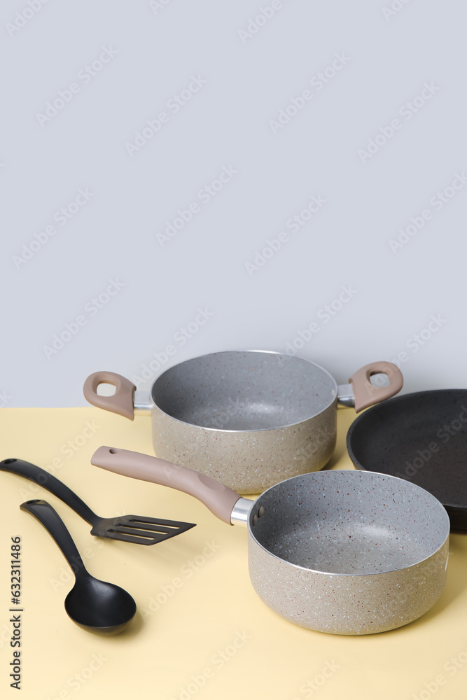 Cooking pots, frying pan and kitchen utensils on color background