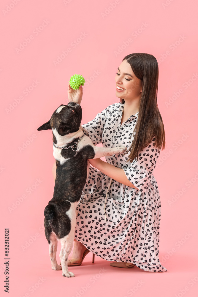 Young woman playing with her French bulldog on pink background