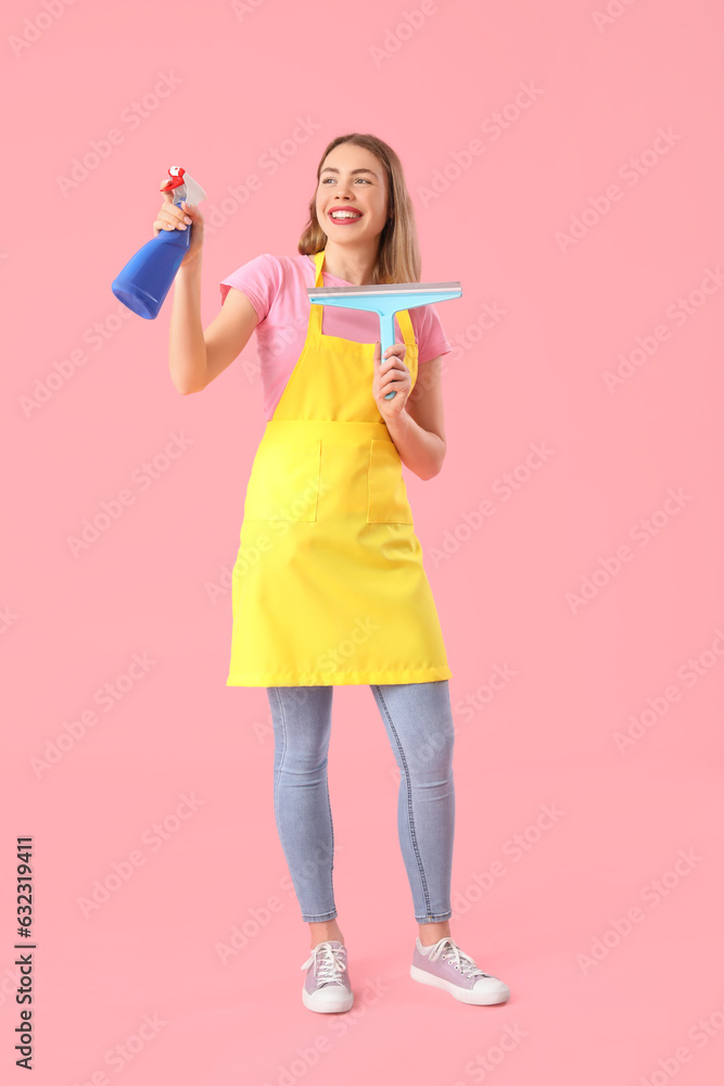 Young woman with bottle of detergent and squeegee on pink background
