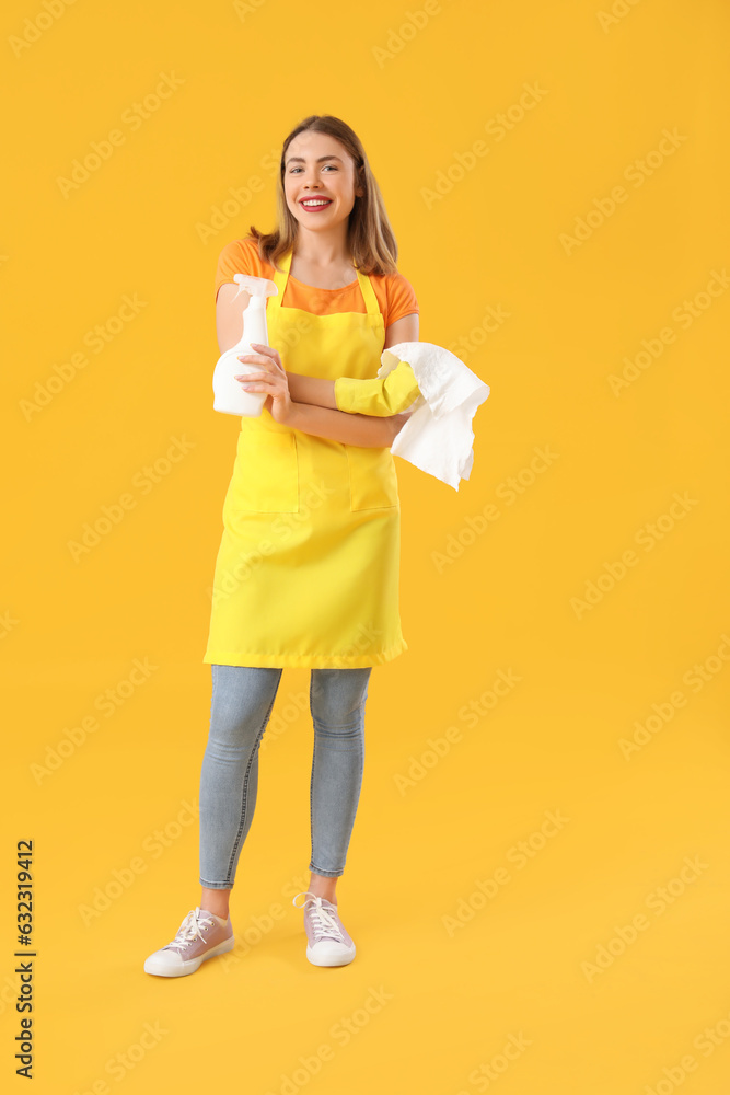 Young woman with bottle of detergent and rag on orange background