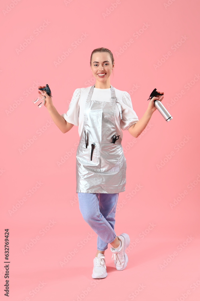 Female hairdresser with spray bottles on pink background
