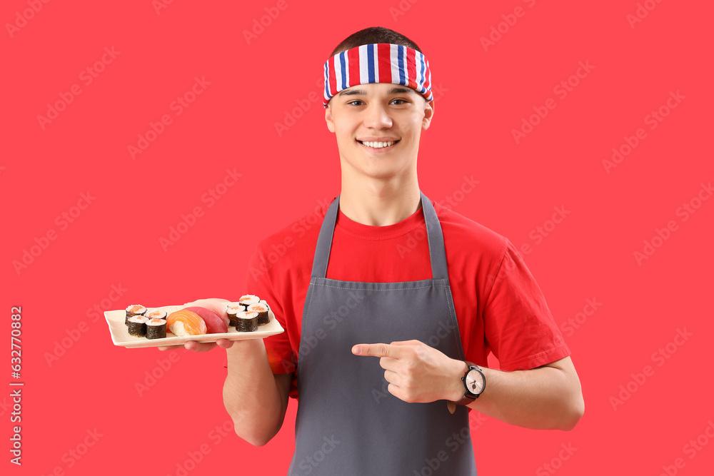 Young man in apron and with tasty sushi on red background