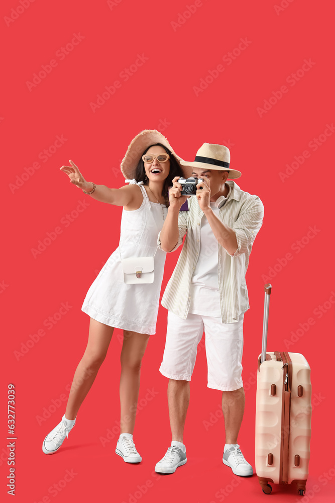 Young couple with photo camera and suitcase on red background