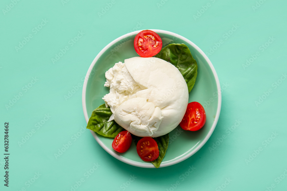 Plate of tasty Burrata cheese with basil and tomatoes on turquoise background