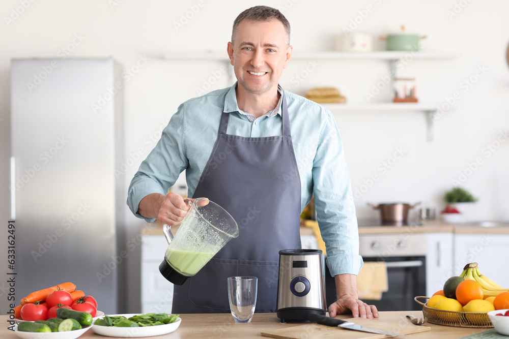 Mature man pouring fresh smoothie from blender into glass in kitchen
